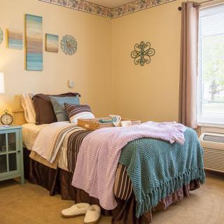 A cozy, well-decorated bedroom with a neatly made bed and soft, pastel-colored blankets.