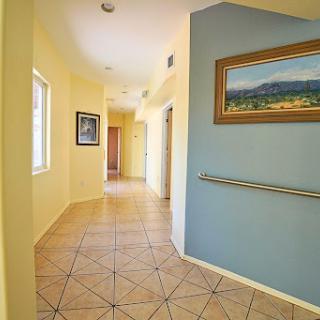 A well-lit hallway featuring a blend of yellow and blue walls, adorned with artwork and tile flooring.