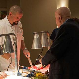 A chef is carving meat at a buffet station while guests are being served.