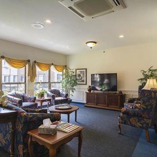 A cozy living room featuring comfortable seating, a television, and natural light streaming through large windows with draped curtains.