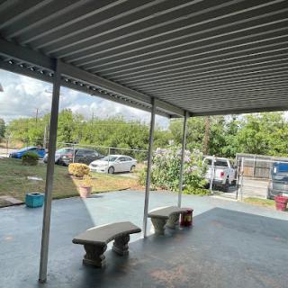 A covered outdoor patio area with benches, overlooking a parking space and greenery.