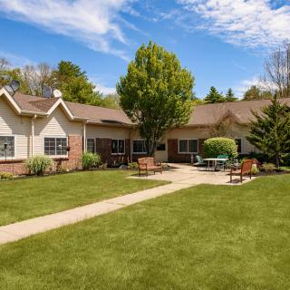 A cozy house with a spacious lawn and outdoor seating under a partly cloudy sky.