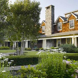 A beautiful house with a lush garden and stone chimney, surrounded by greenery.