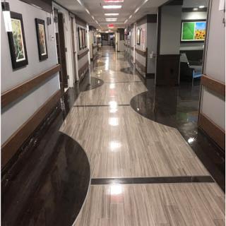 A well-lit hospital hallway featuring modern flooring and framed artwork on the walls.