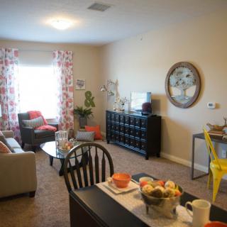 A cozy living room with a sofa, coffee table, and a television, complemented by decorative elements and a small dining area.