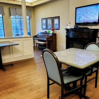 A cozy dining area with a television and piano, featuring tables and chairs on a wooden floor.