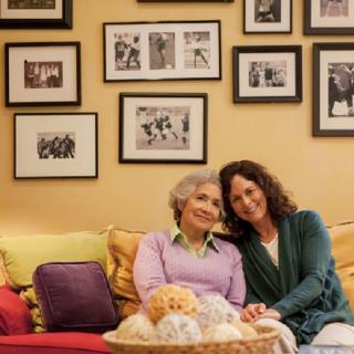 Two people sitting together on a couch, surrounded by framed photos on the wall.