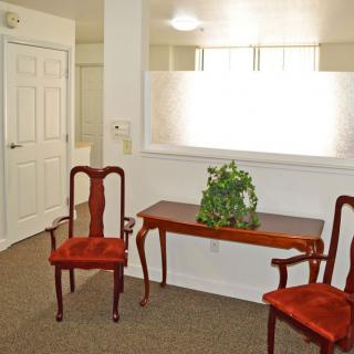 A cozy waiting area with two red upholstered chairs, a wooden table, and a potted plant under soft lighting.