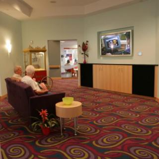 A cozy lobby with vibrant carpet, a couch, and a television on the wall.
