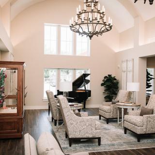 A spacious and elegantly designed living room featuring a grand piano, plush armchairs, and a decorative chandelier.