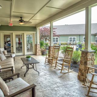 A cozy covered porch with rocking chairs and outdoor seating, surrounded by plants.