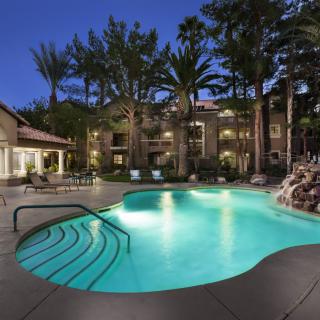 A serene outdoor pool area illuminated at night with palm trees in the background.
