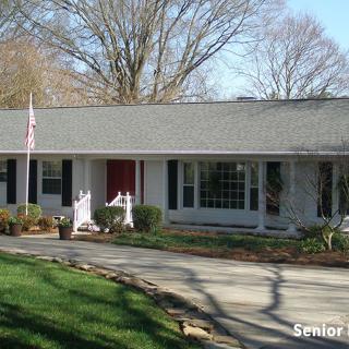 A ranch-style house with a red door and white exterior, surrounded by trees and a well-maintained lawn.