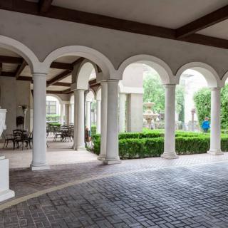 A serene courtyard with archways and white columns, featuring greenery and outdoor seating.