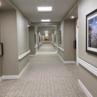 A long, carpeted hallway with framed artwork on the walls and ceiling lights.