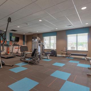 A well-equipped gym with exercise machines, weights, and large windows providing natural light.