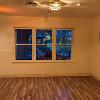 A cozy room featuring large windows and warm lighting, showcasing the wooden floor.