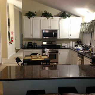 A modern kitchen with white cabinets and a spacious countertop, featuring various appliances and a small dining area.