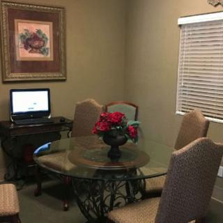 A cozy dining room with a glass table, upholstered chairs, and a computer on the side.
