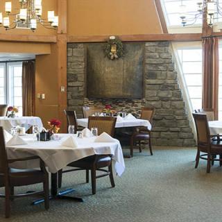 A cozy restaurant dining area with neatly set tables and chairs, featuring a stone accent wall and large windows.