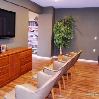 A cozy waiting area featuring comfortable chairs, a wooden cabinet, and a television, complemented by a decorative plant.