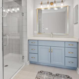 A modern bathroom with a blue vanity, large mirror, and glass shower enclosure.