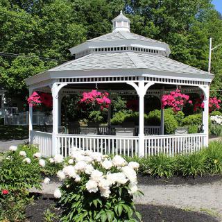 A charming white gazebo surrounded by vibrant flowers in a lush garden setting.