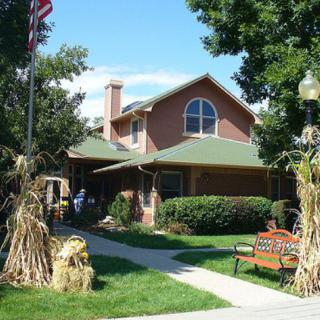 A charming house with a green roof, surrounded by lush landscaping and adorned with autumn decorations.