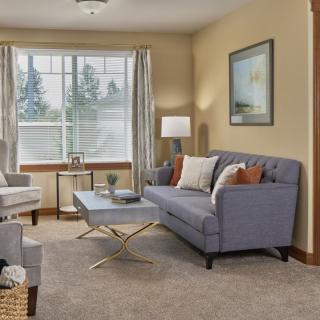 A cozy living room featuring a sofa, armchair, and coffee table with a large window letting in natural light.