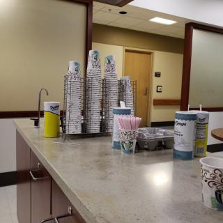 A coffee station in a clinic waiting area with stacks of paper cups arranged on a countertop.