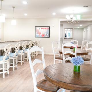 A bright and modern restaurant interior with wooden tables, white chairs, and blue floral centerpieces.