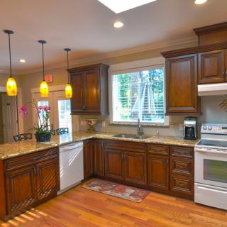 A spacious kitchen featuring wooden cabinets, granite countertops, and modern appliances, illuminated by pendant lights and natural light from a skylight.