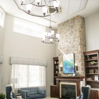 A spacious living room with a vaulted ceiling, featuring a stone fireplace, elegant chandelier, and ample natural light.