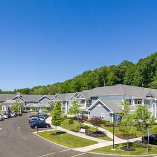 A view of a suburban apartment complex with well-maintained landscaping and ample parking under a clear blue sky.