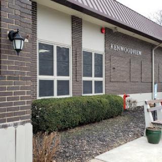 The exterior of a brick building featuring multiple windows, landscaping, and a light fixture.