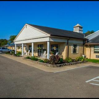 A charming building featuring a welcoming porch, surrounded by well-maintained landscaping and a clear blue sky.