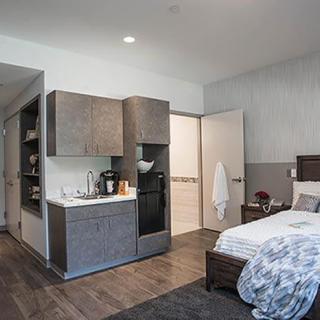 A modern apartment bedroom with a kitchenette and minimalist decor.
