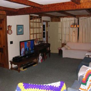 A cozy living room with a television, sofas, and wooden ceiling beams.