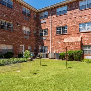 A sunny courtyard of a brick apartment building with a well-maintained lawn.