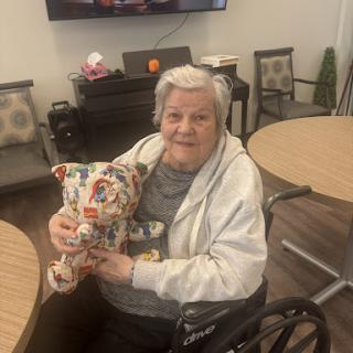 An elderly woman in a wheelchair joyfully holding a colorful stuffed animal in a care facility.