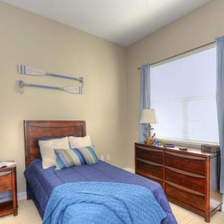 A cozy bedroom with a single bed featuring blue bedding, a wooden dresser, and a window with curtains.
