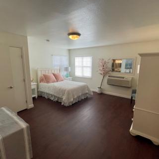 A well-lit bedroom with a bed, mirror, and dresser on a hardwood floor.