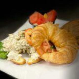 A delicious croissant sandwich with chicken salad and a side of fruit.