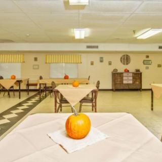 A community dining room with tables set for autumn, each featuring a small pumpkin centerpiece.