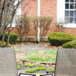 Two chairs facing a brick building with shrubs and a window in the background.