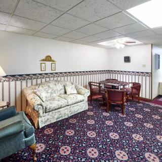 A vintage-style living room featuring a floral sofa, wooden table with chairs, and patterned carpet.
