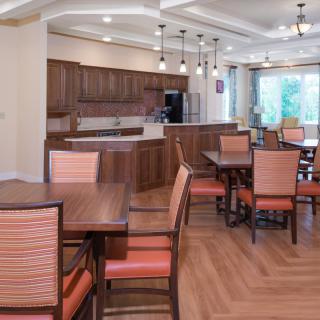 A modern dining and kitchen area with wooden tables and chairs, pendant lighting, and a hardwood floor.