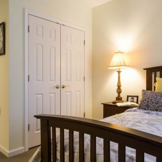 A cozy bedroom with a wooden bed, nightstand, and lamp next to a closet.