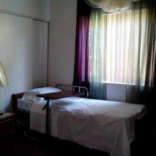 A simple hospital room with a bed and curtains filtering daylight.