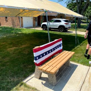 A wooden bench adorned with a red, white, and blue fabric under a tent, perfect for a summer gathering.